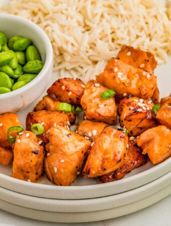 Close up square image of salmon on stacked plates with rice and edamame.