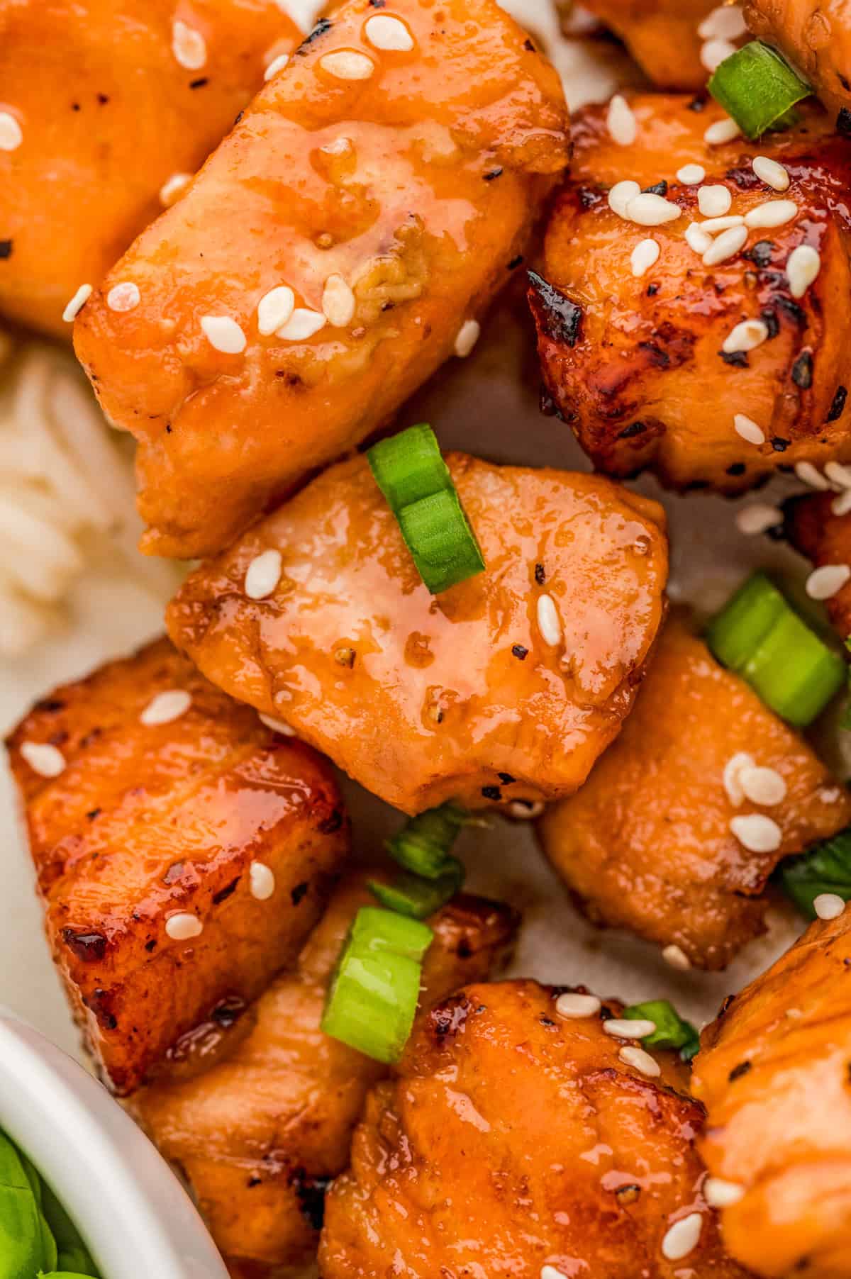 Close up of salmon showing the sauce, sesame seeds and green onions.