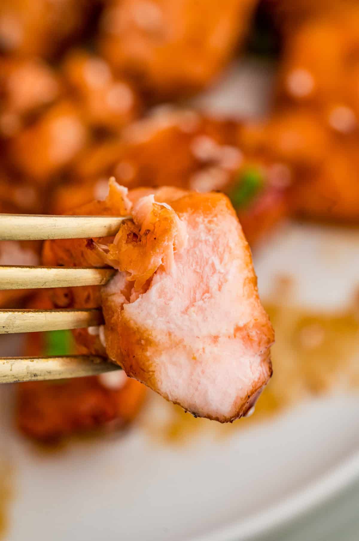 Fork holding up a piece of salmon with a bite taken out of it.