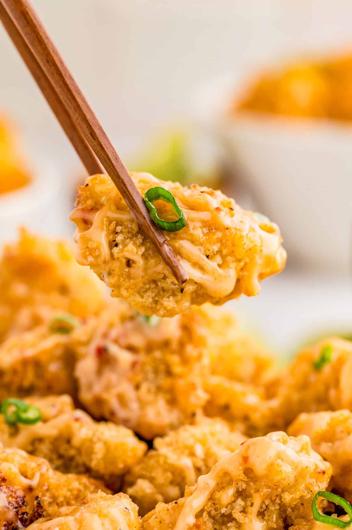 Chopsticks holding up one piece of chicken.