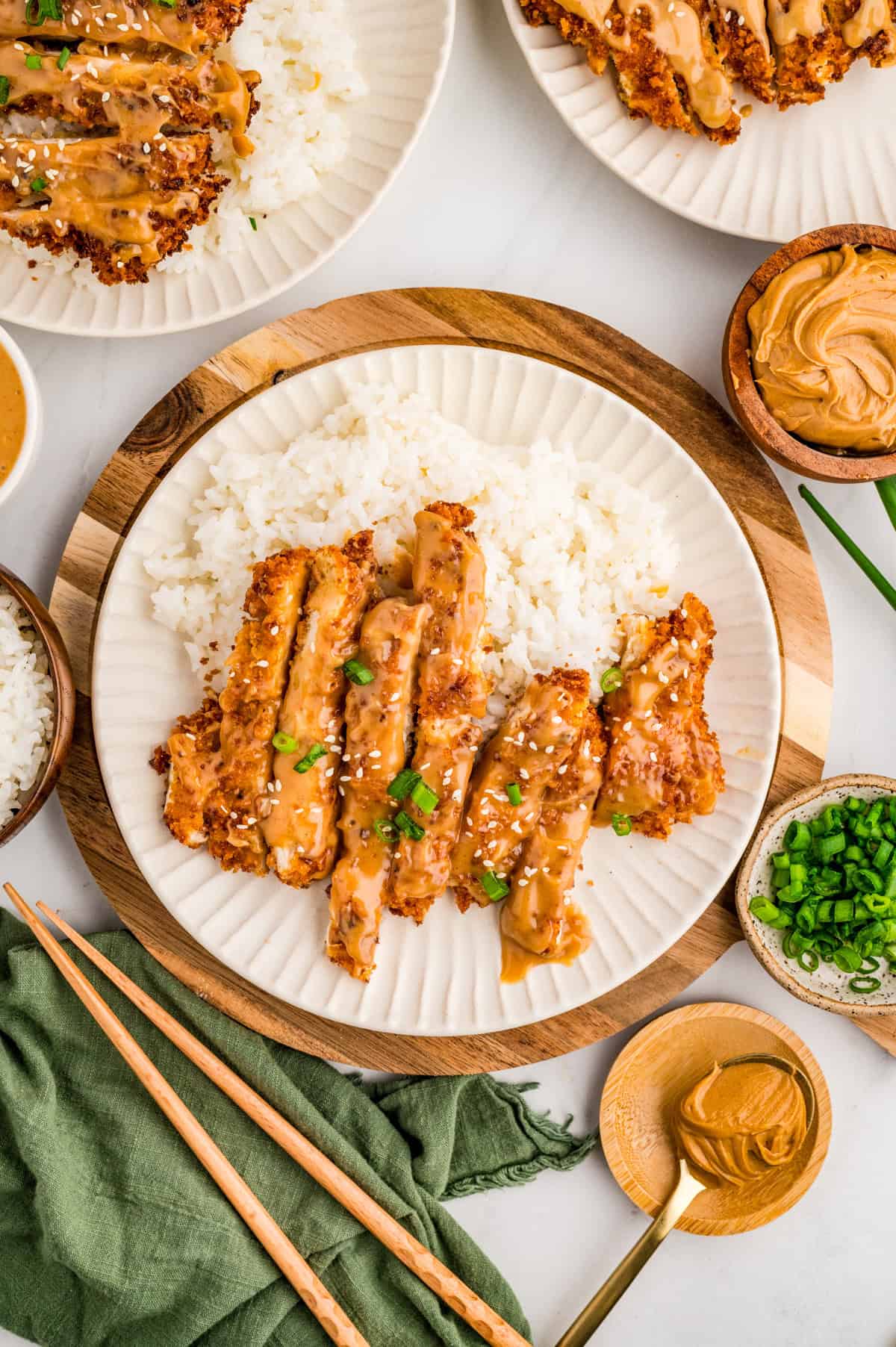 Overhead of finished chicken on plate over rice with garnishes. With peanut butter, chopstick and green onions by plate.