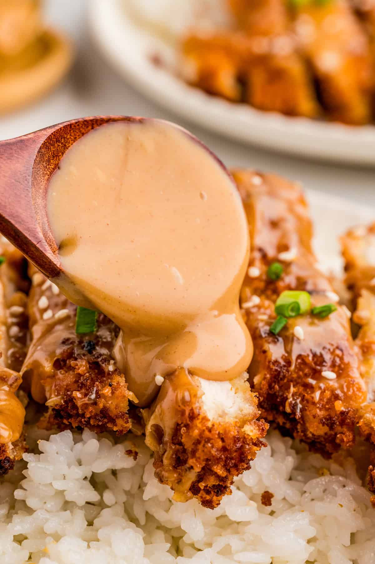 Spoon drizzling peanut sauce over chicken.