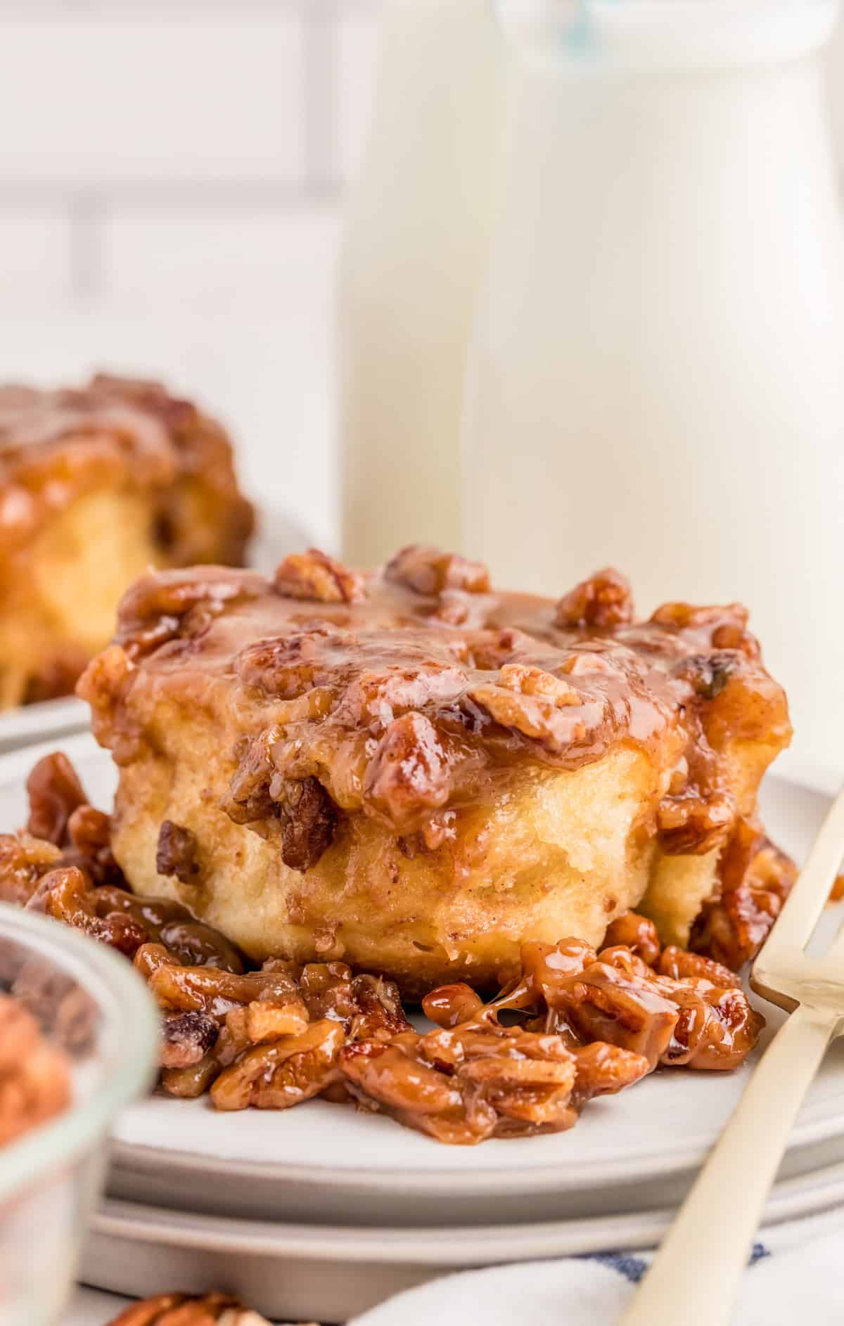 One of the Pecan Sticky Buns on stacked white plates with the pecan mixture on plate and top.