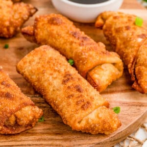 Square image of finished egg rolls on wooden board with green onions.