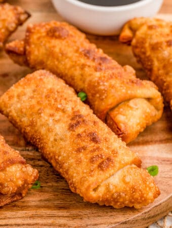 Square image of finished egg rolls on wooden board with green onions.