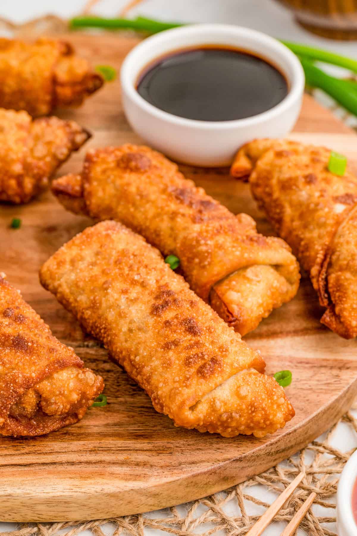 Pork Egg Rolls on round wooden board with green onions and a bowl of soy sauce.