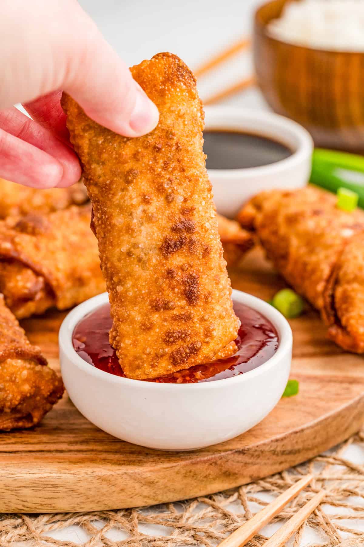 Hand dipping one of the egg rolls into sweet and sour sauce.