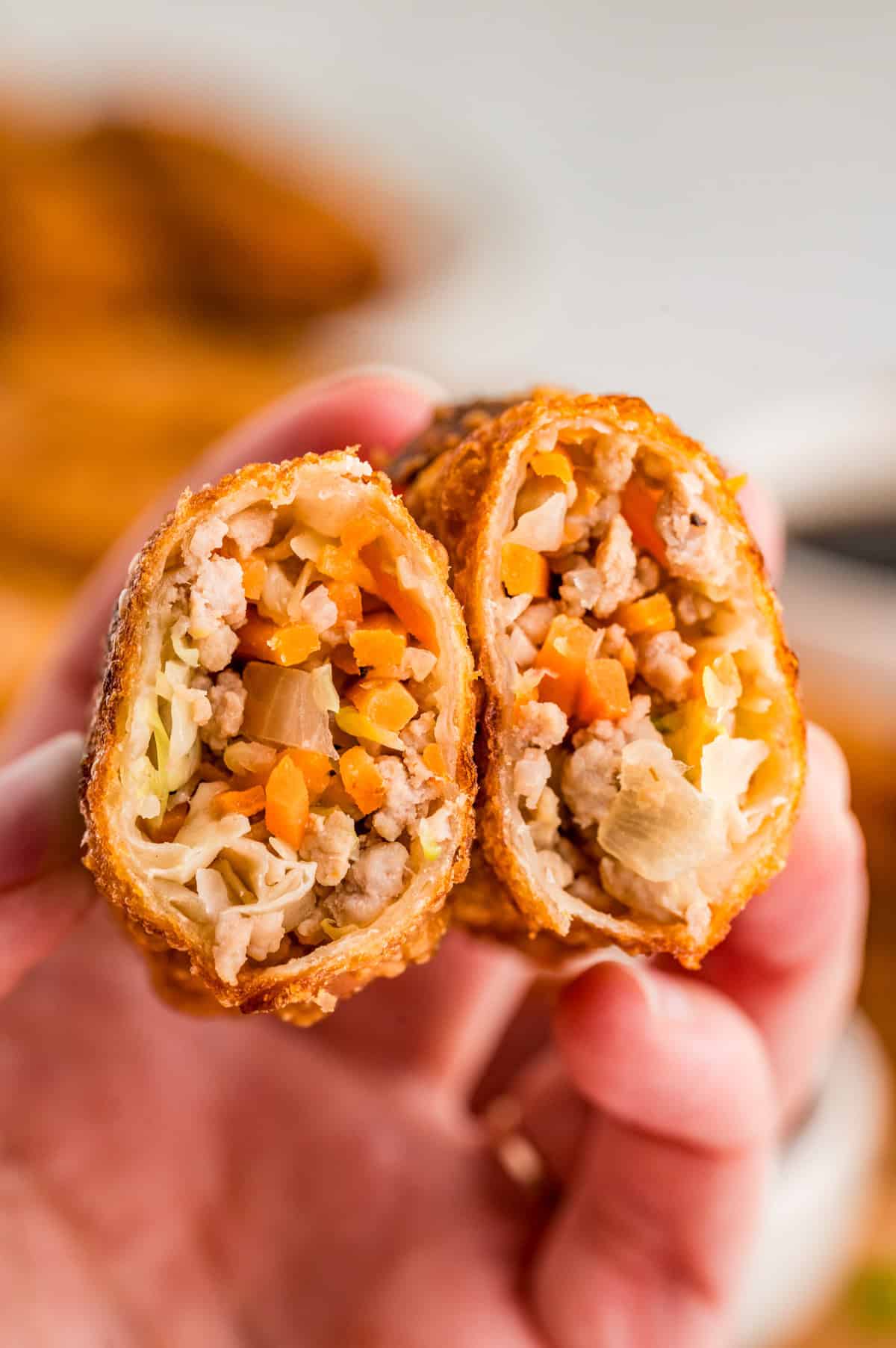 Hand holding one egg roll cut in half showing the filling inside.