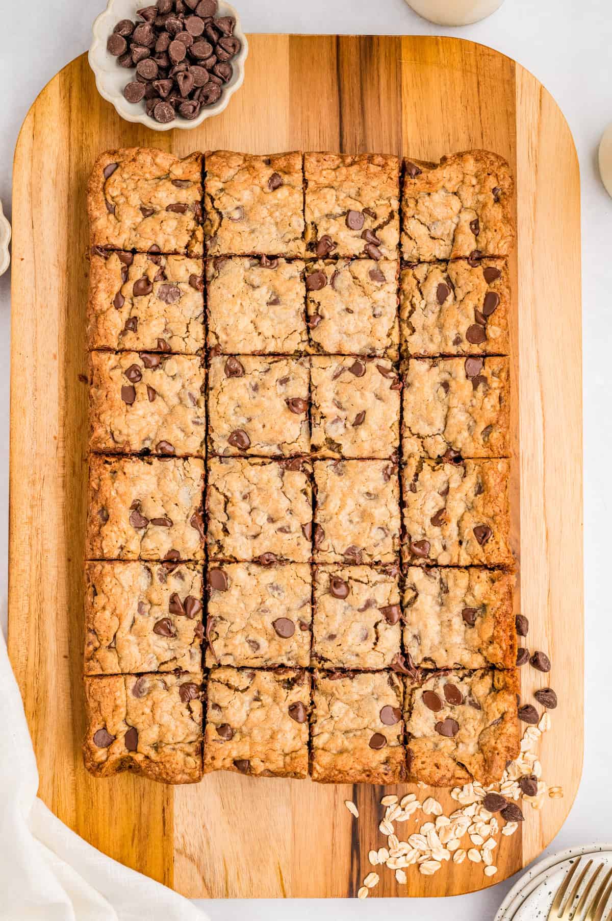 Overhead of cut bars on wooden board with chocolate chips and oats beside them.