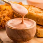 Close up of sauce in wooden bowl with spoon drizzling sauce into bowl.