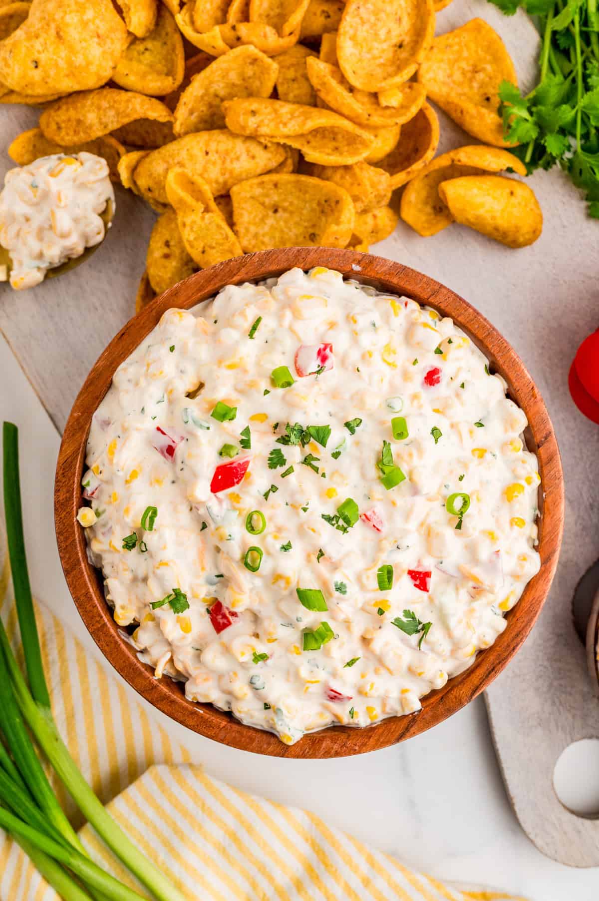 Overhead of dip in wooden bowl topped with green onions and surrounded by chips.