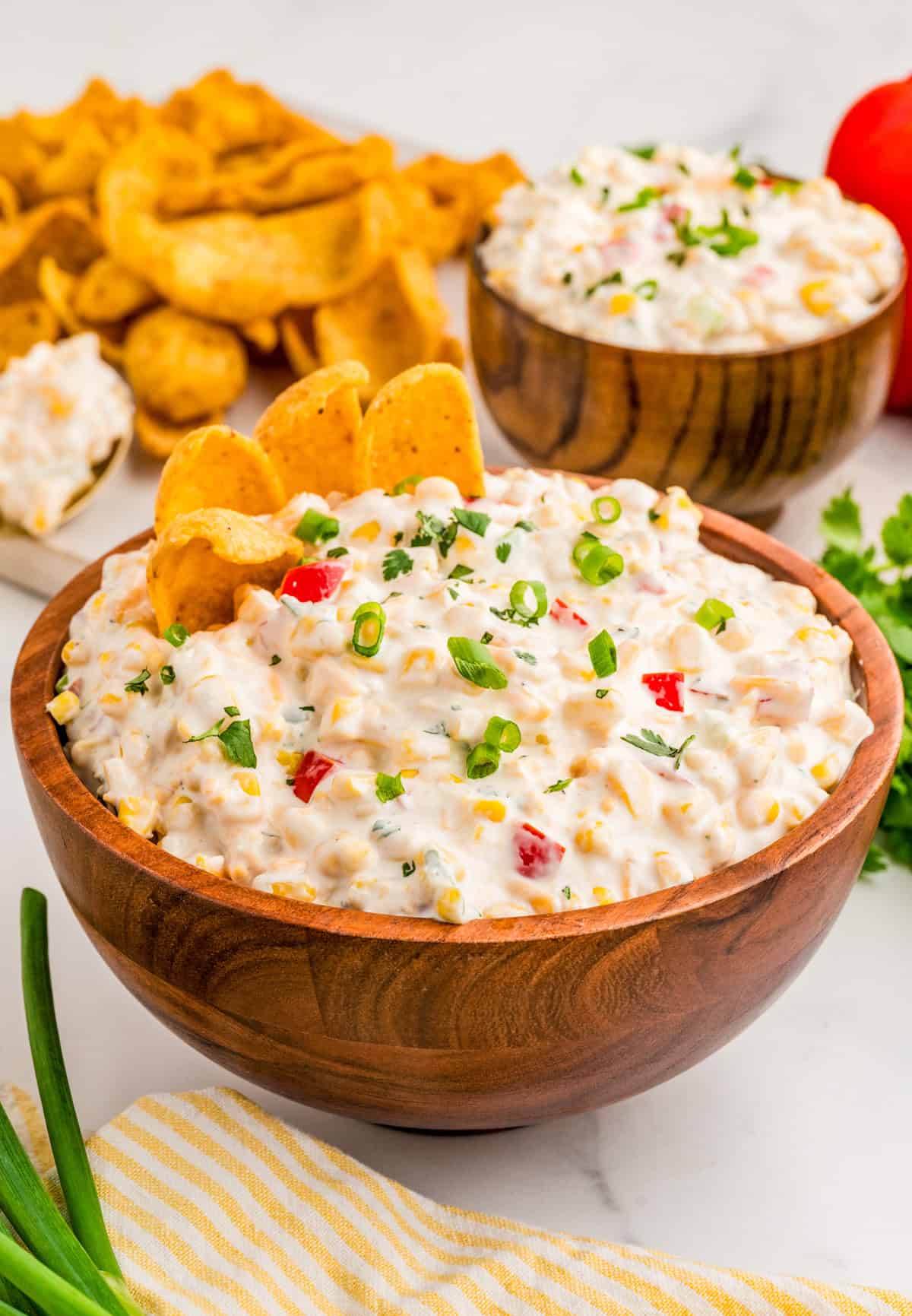 Corn Dip in wooden bowl topped with green onions and chips in dip with chips and more dip in background.