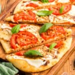 Close up square image of pizza cut into triangles on wooden cutting board.