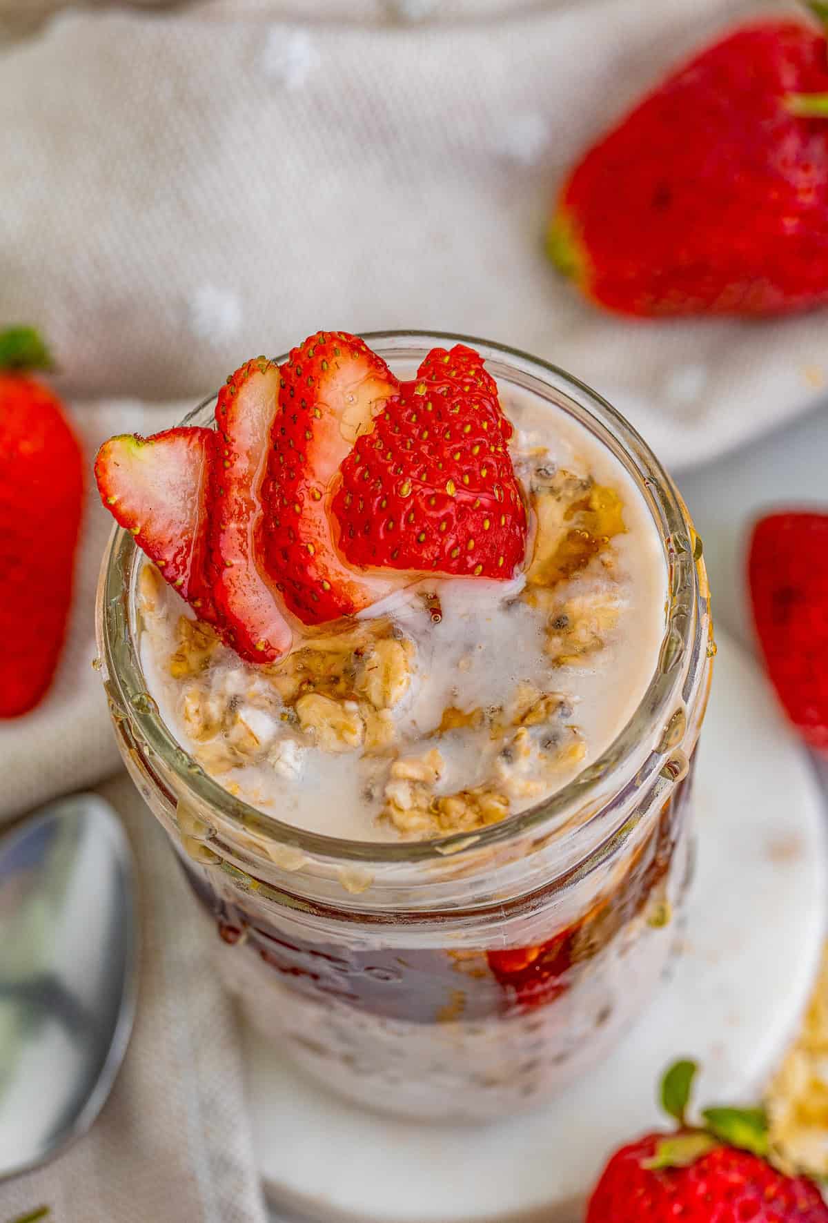 Overhead photo of oats on marble coaster topped with sliced strawberries and honey.