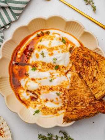 Overhead square image of eggs over yogurt and garnished with spiced butter and toast.