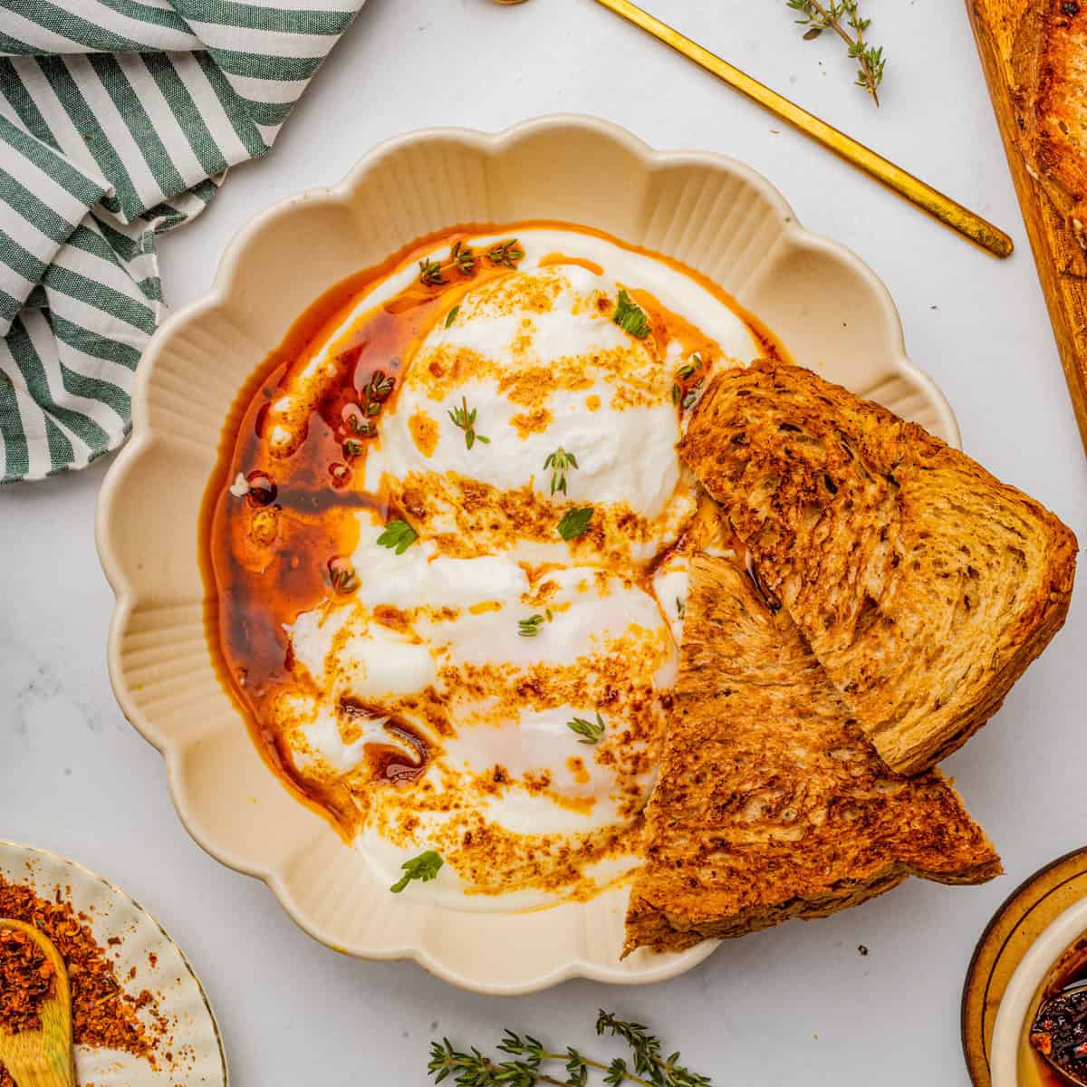 Overhead square image of eggs over yogurt and garnished with spiced butter and toast.