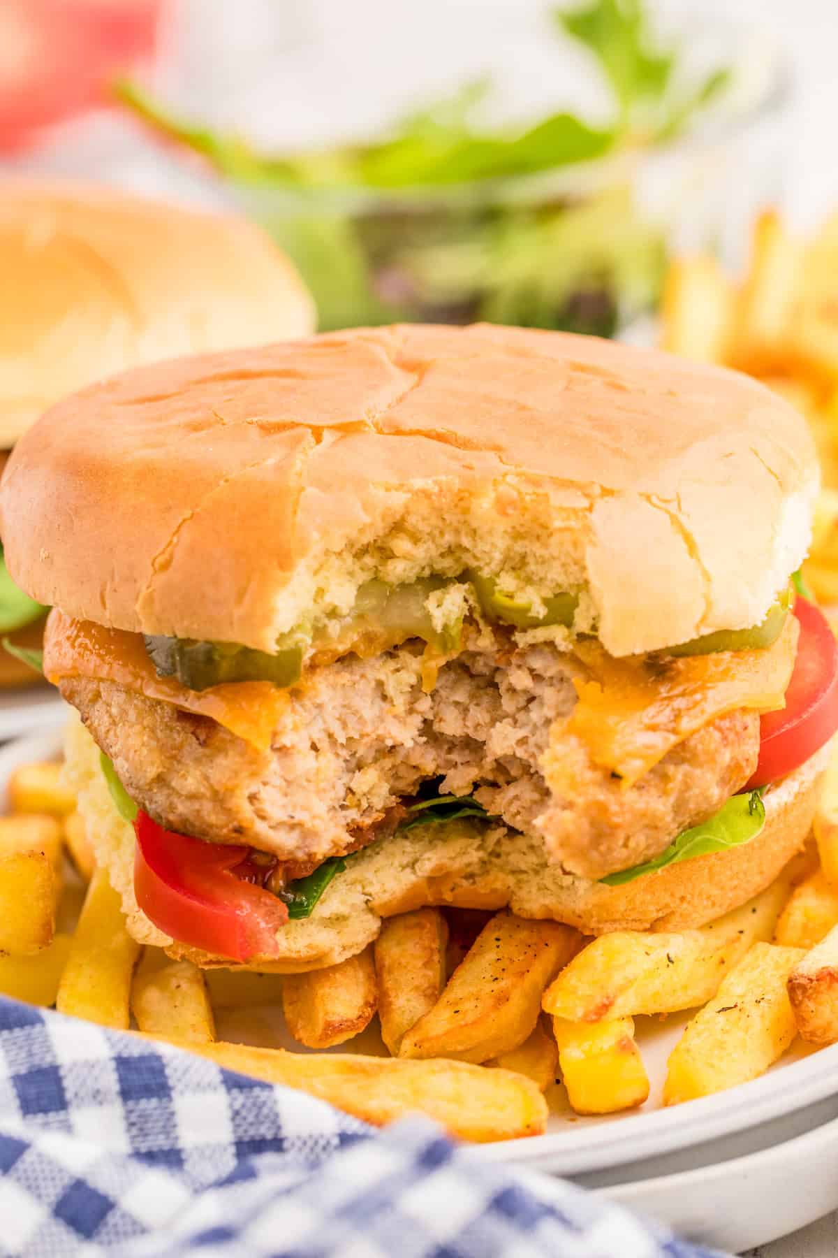 Burger on top of a plate of fries with bite taken out of it.