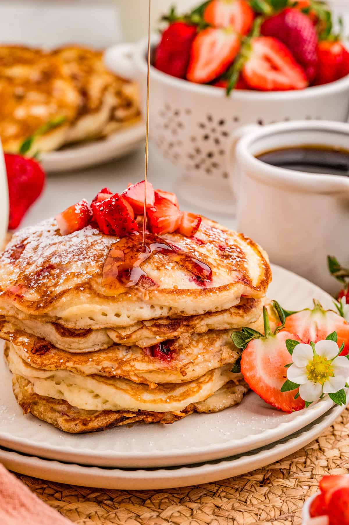 Pancakes stacked on plates with syrup being poured over pancakes.