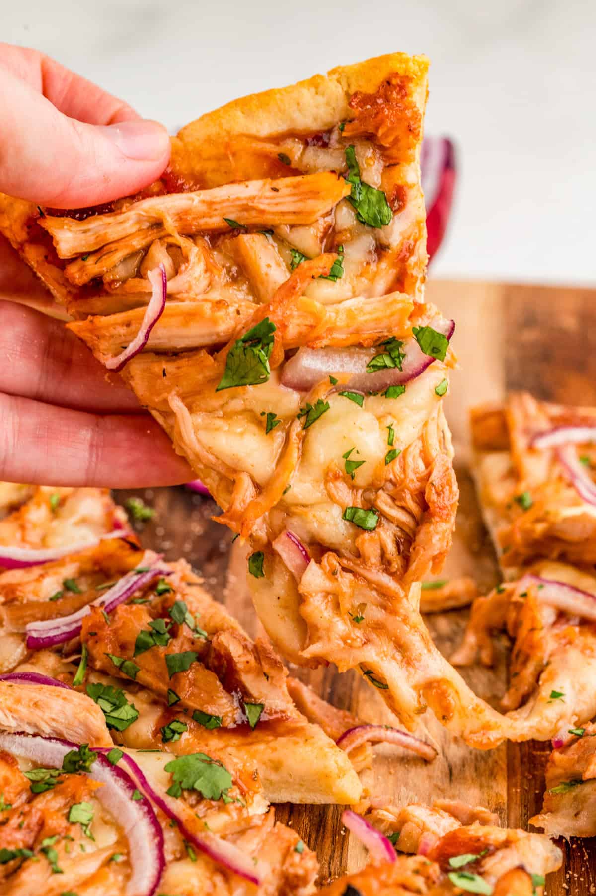 Hand holding up one slice of pizza showing the toppings and a cheese pull.