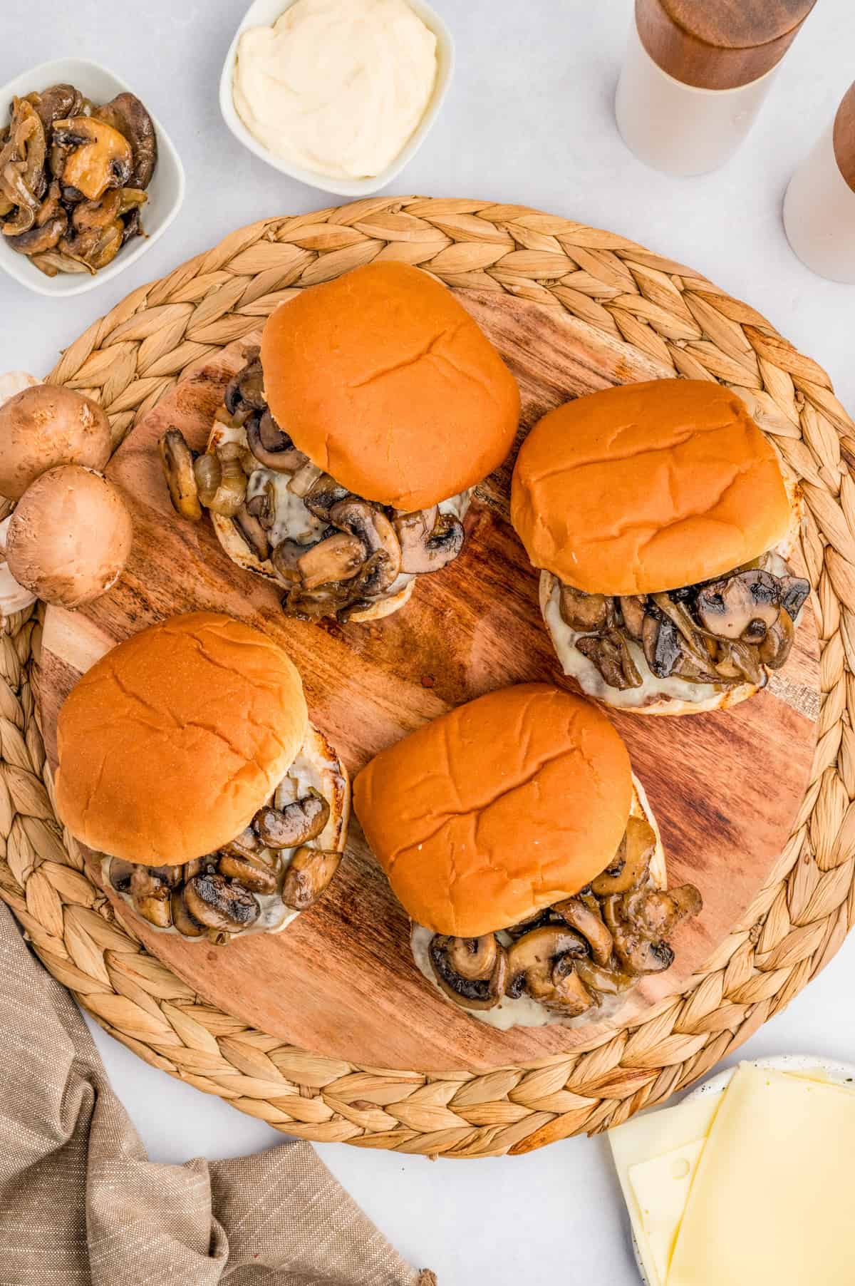Overhead of finished burgers on a wooden board on a wicker trivet.