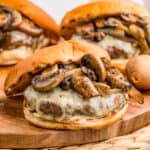 Square image of burgers on wooden board with mushrooms and melted cheese.