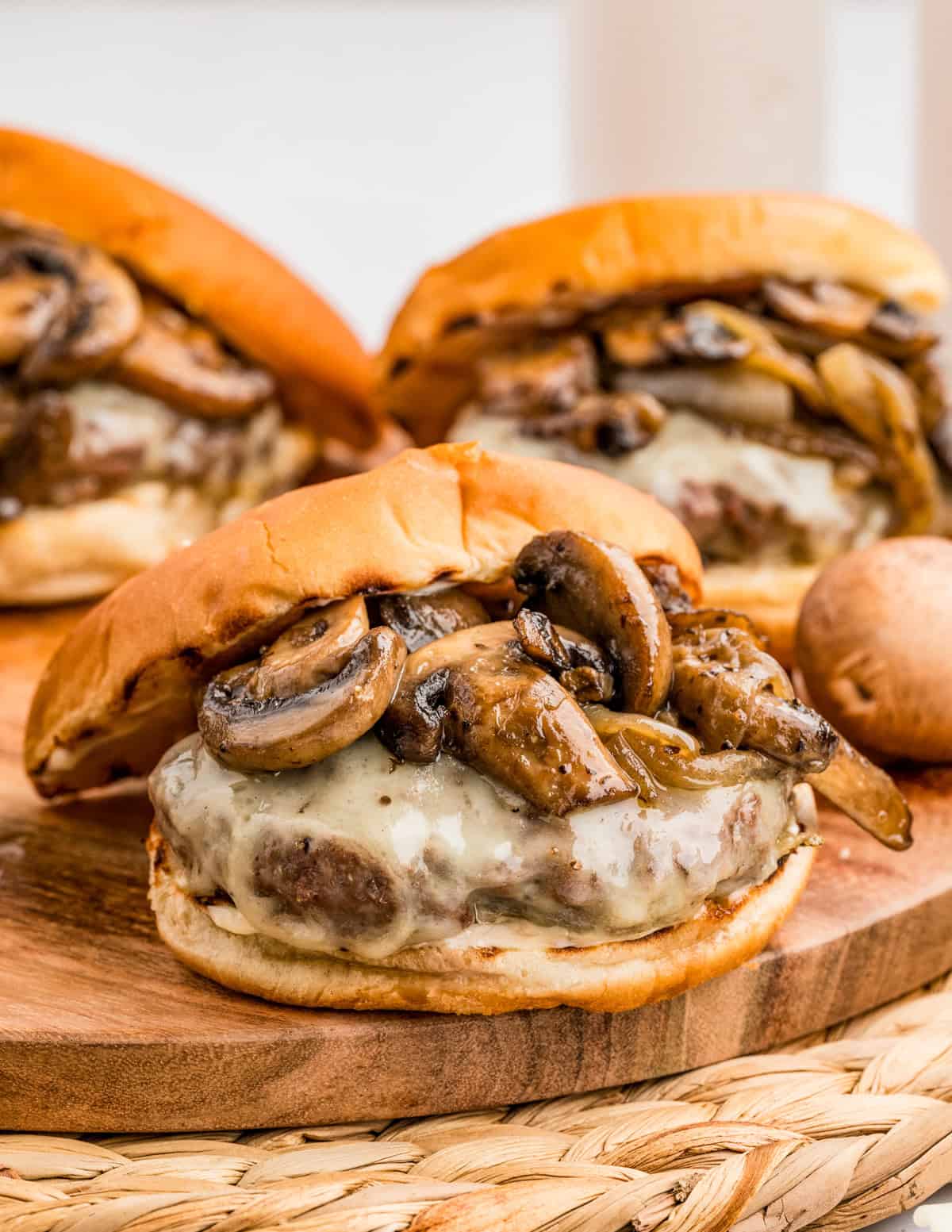 Mushroom and Swiss Burger on wooden board with bun slightly off the top showing the sautéed mushrooms and melted cheese.