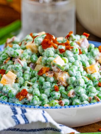 Close up square image of salad in bowl topped with bacon and cheese.