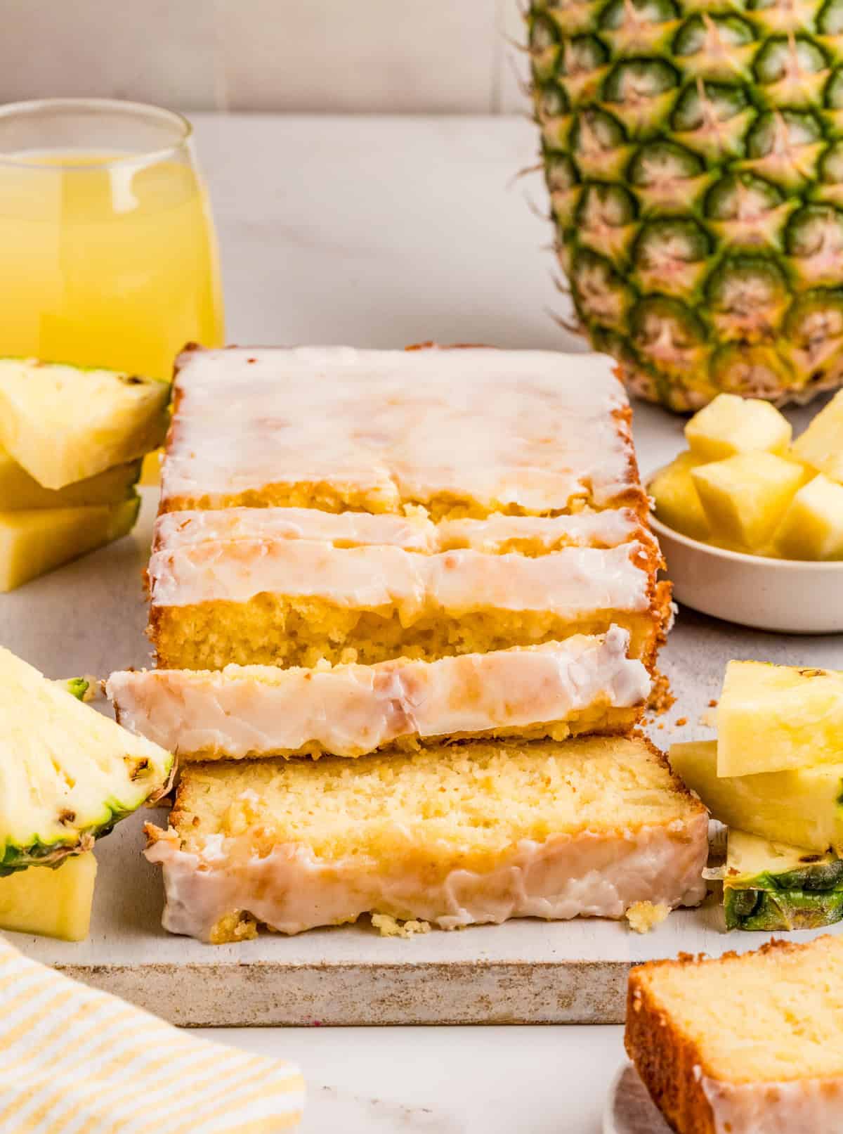 Pineapple Bread sliced on parchment paper, glazed and surrounded by slices of pineapple.
