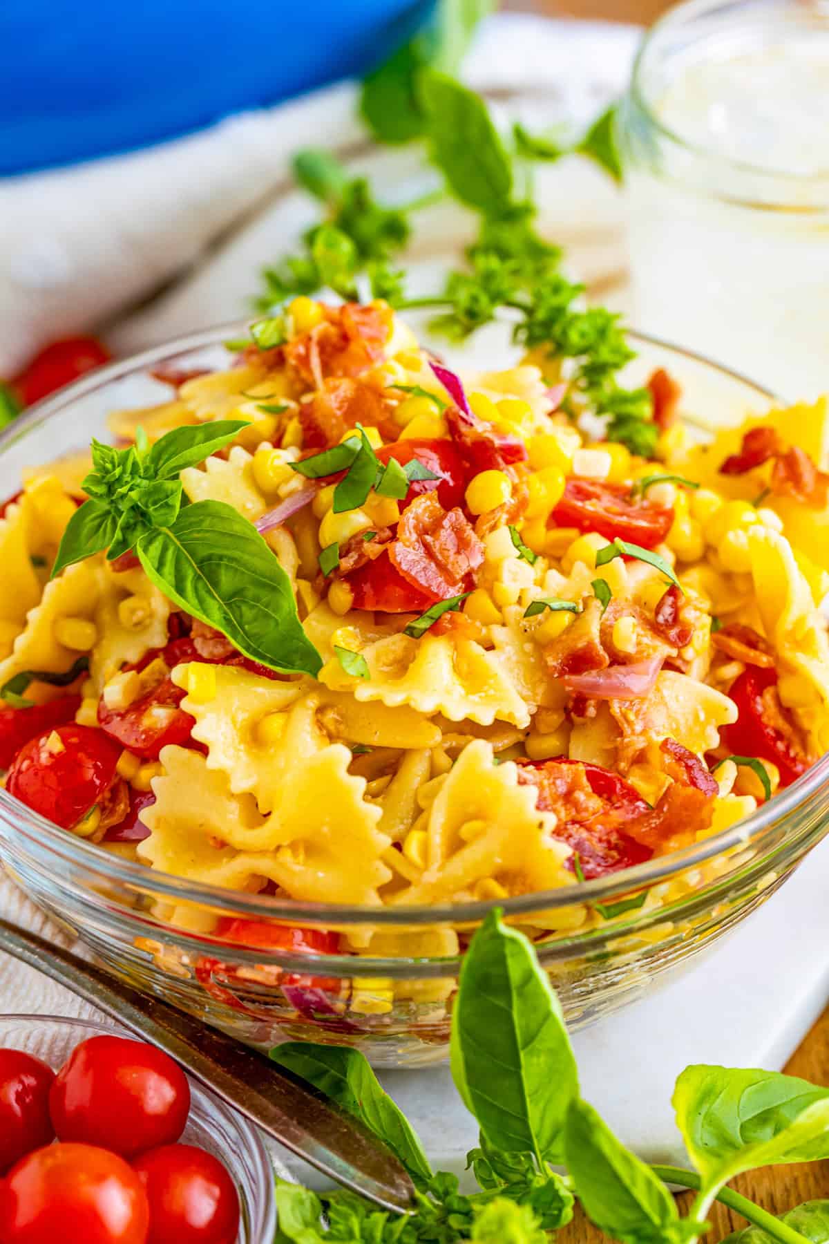Bacon and Corn Pasta Salad in clear bowl mixed up and toped with basil leaves.
