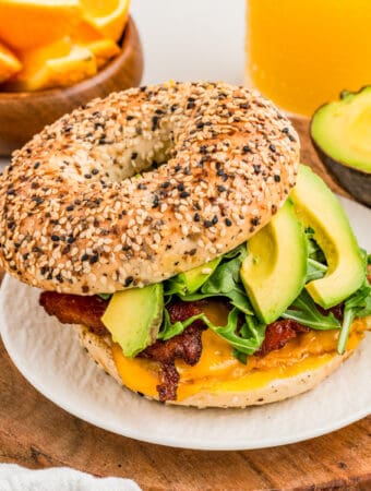 Square image of sandwich on white plate with top bagel off slightly showing the layers of ingredients.