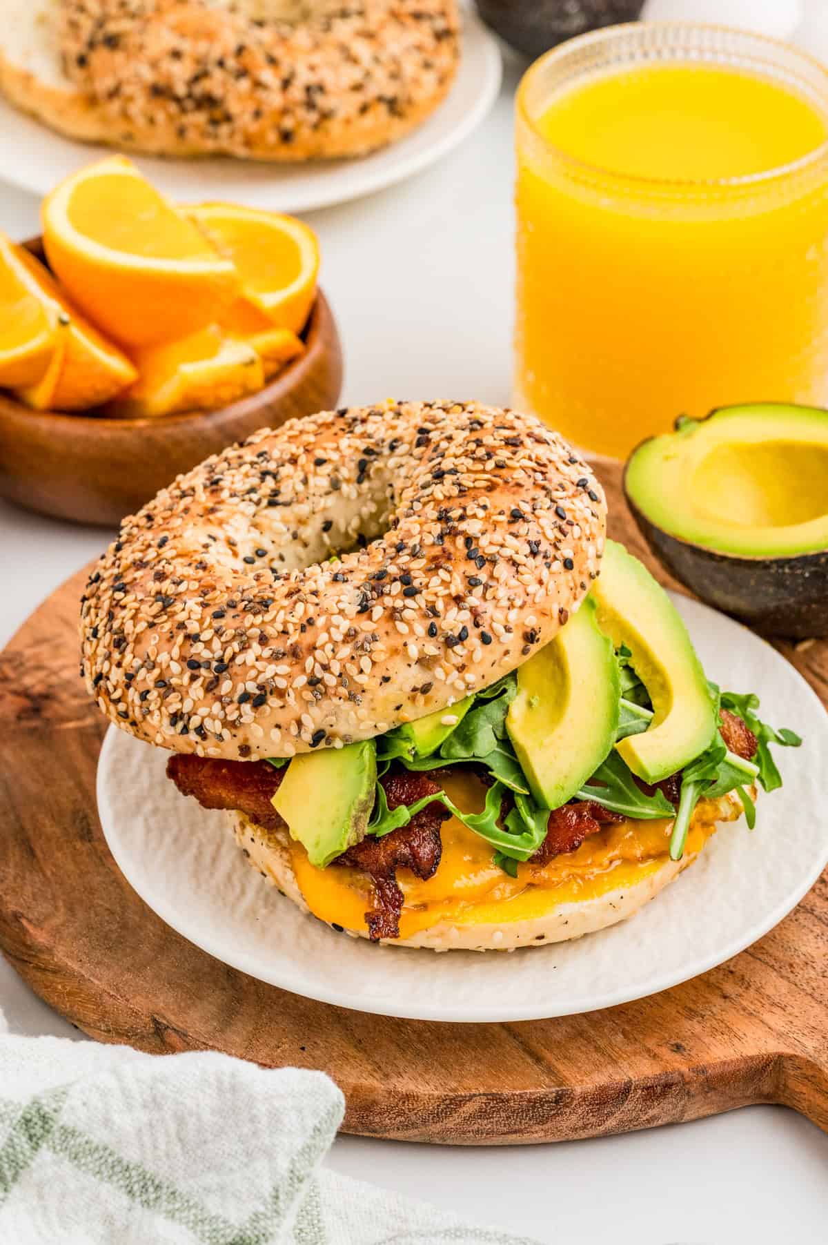 Finished Bagel Breakfast Sandwich on white plate on wooden board. Top slice of bagel off slightly showing the layered ingredients.
