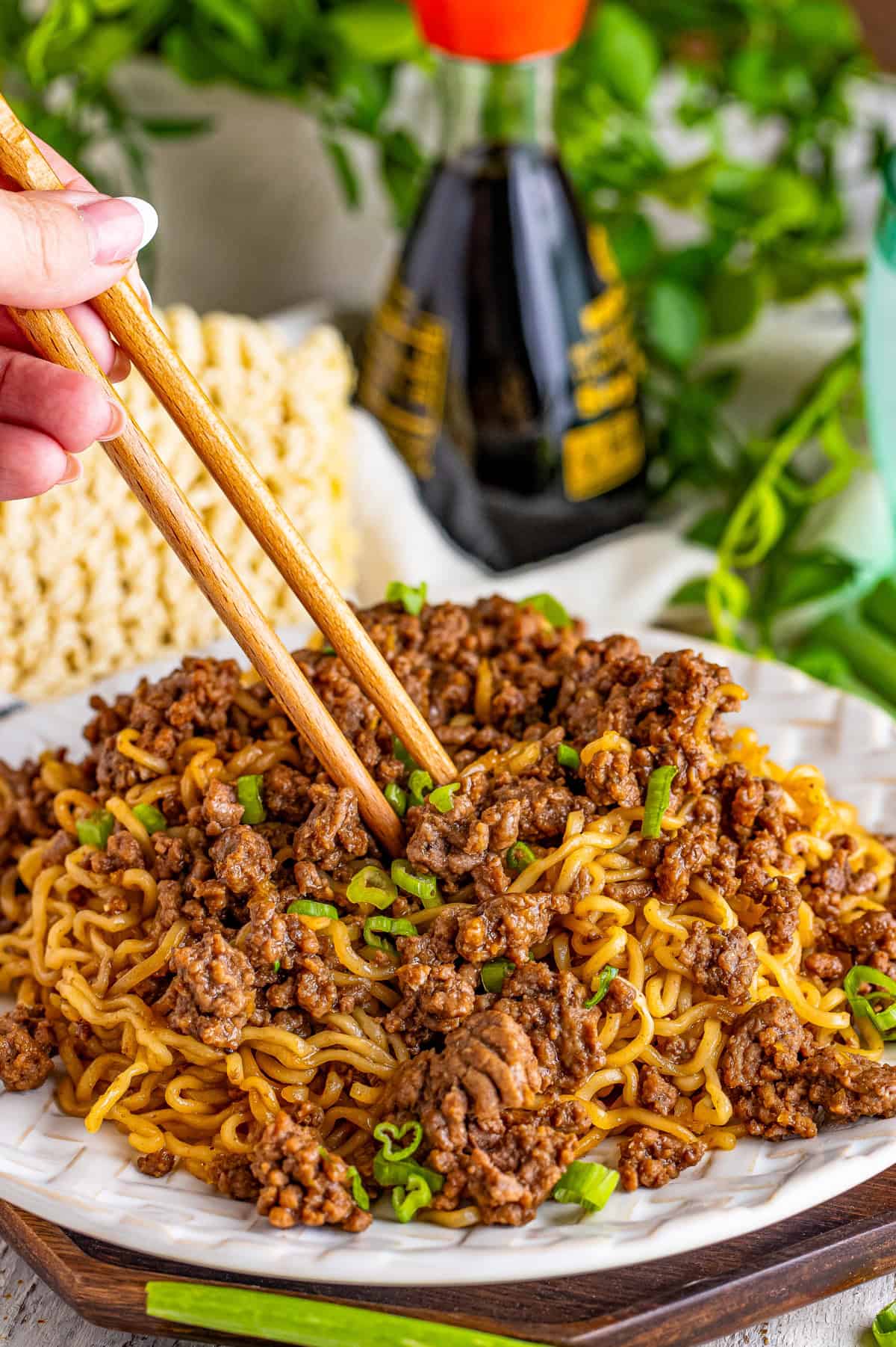 Chop sticks going into ramen on plate topped with green onions.