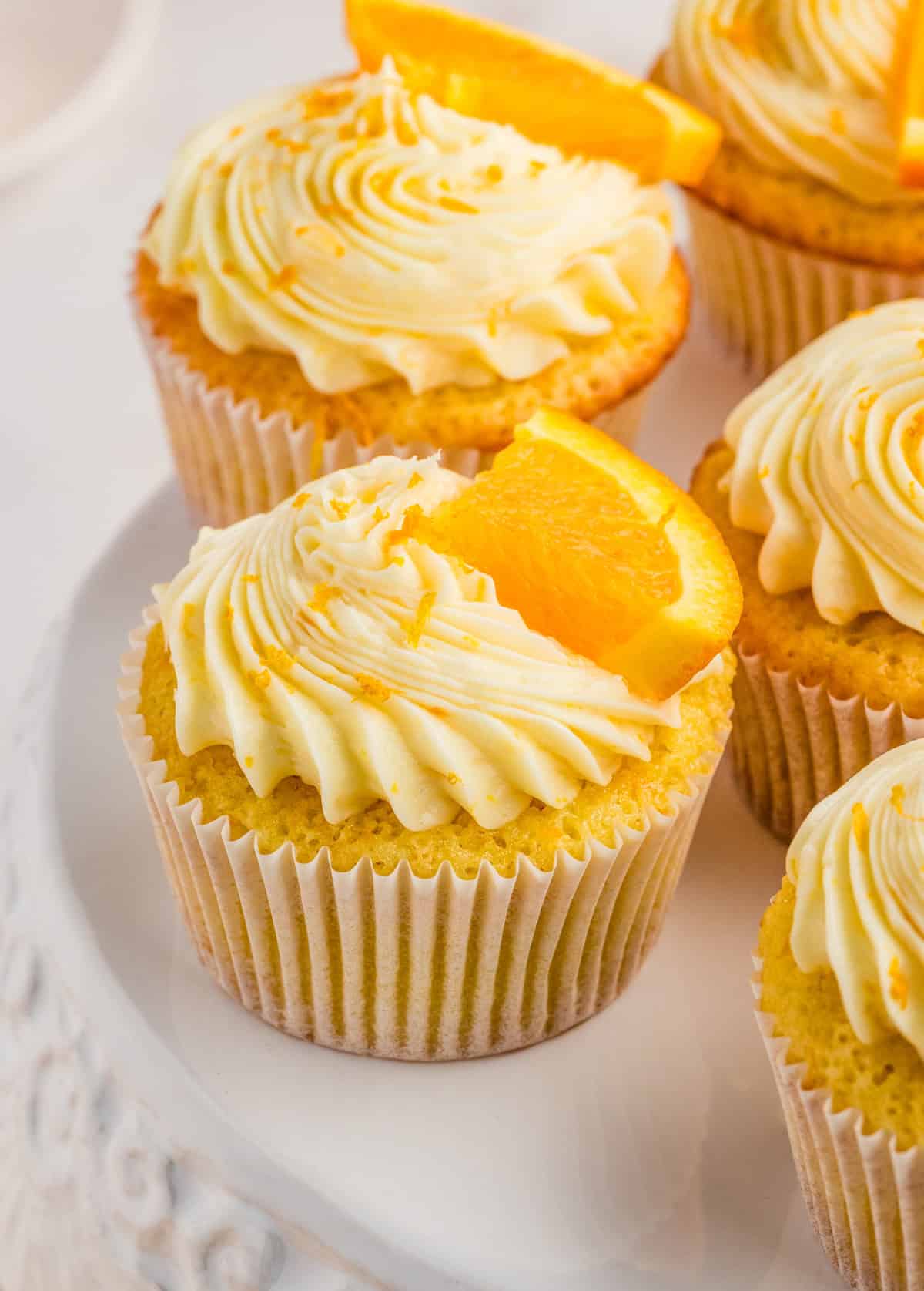 Orange Cupcakes on a cake stand frosted and garnished with orange zest and slice.