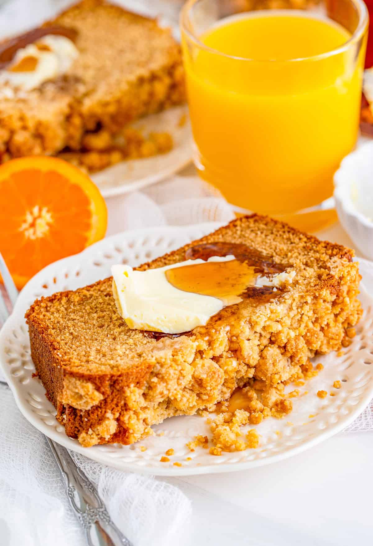 Slice of Pancake Bread on white plate topped with butter and syrup with orange juice and orange in background.