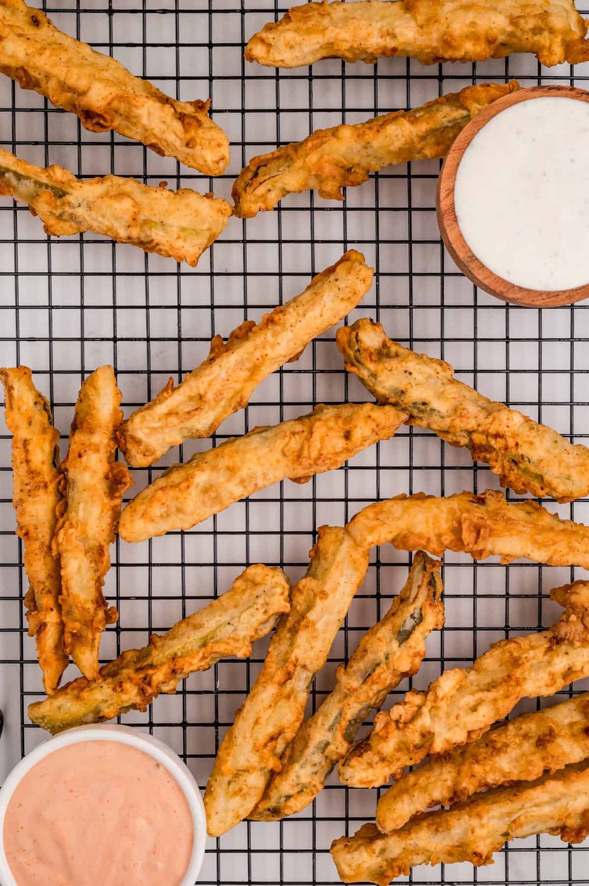 Overhead of finished Pickle Fries on wire rack with dipping sauces.