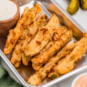 Close up square image of pickles on metal tray with dipping sauces.