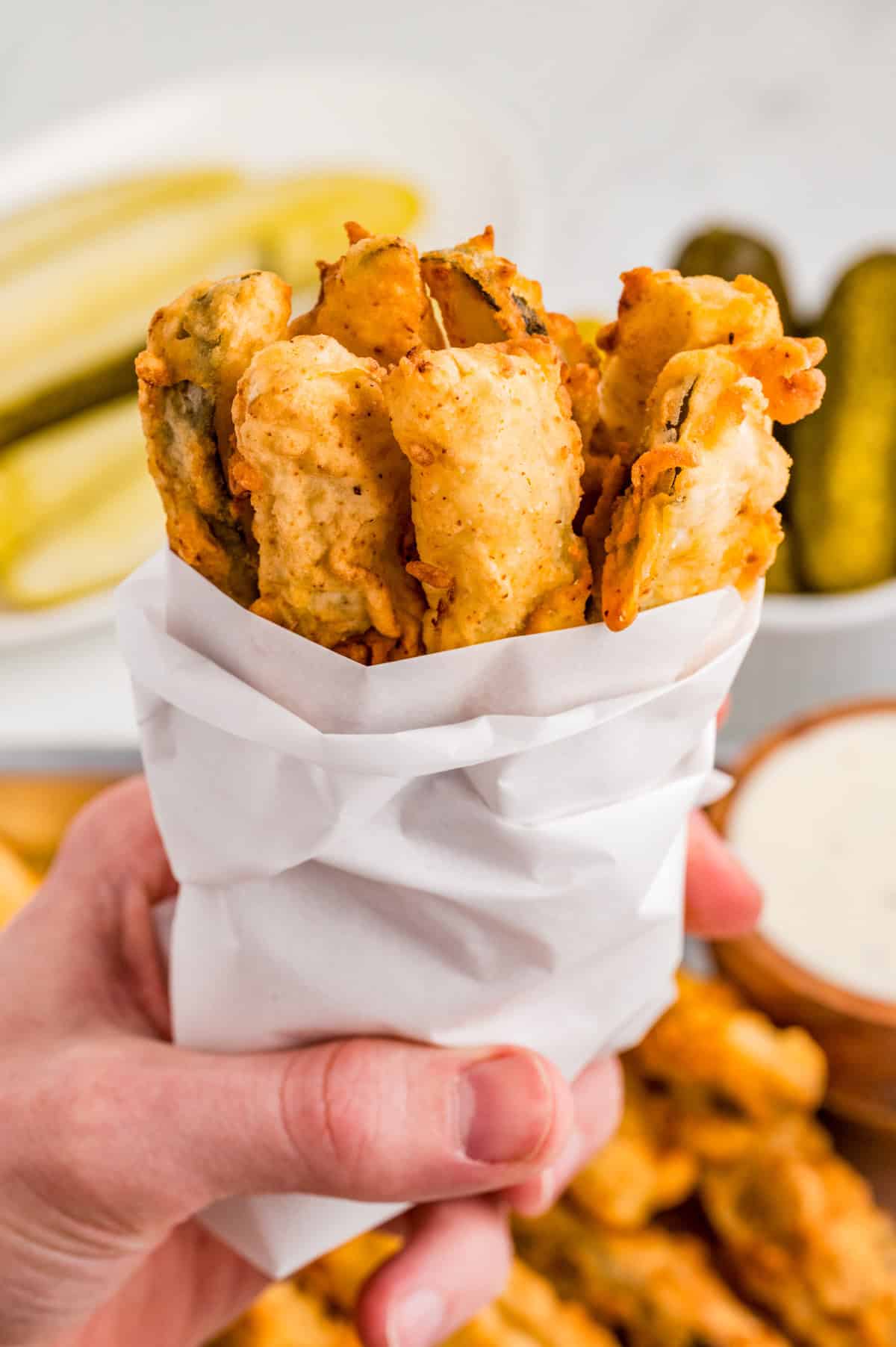 Hand holding up a bunch of pickles wrapped in parchment paper.