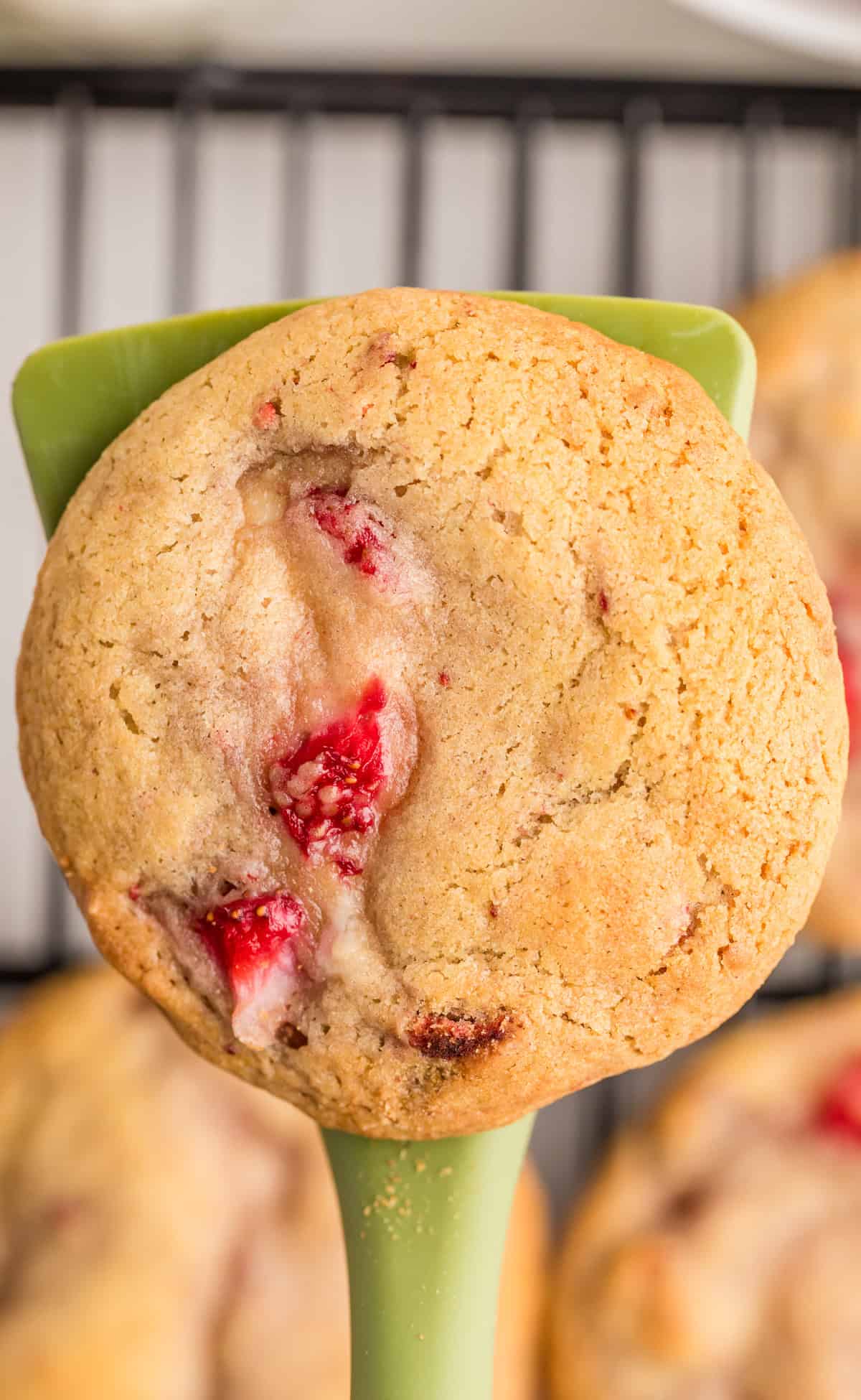 Overhead of one finished cookie being held up from wire rack with spatula.