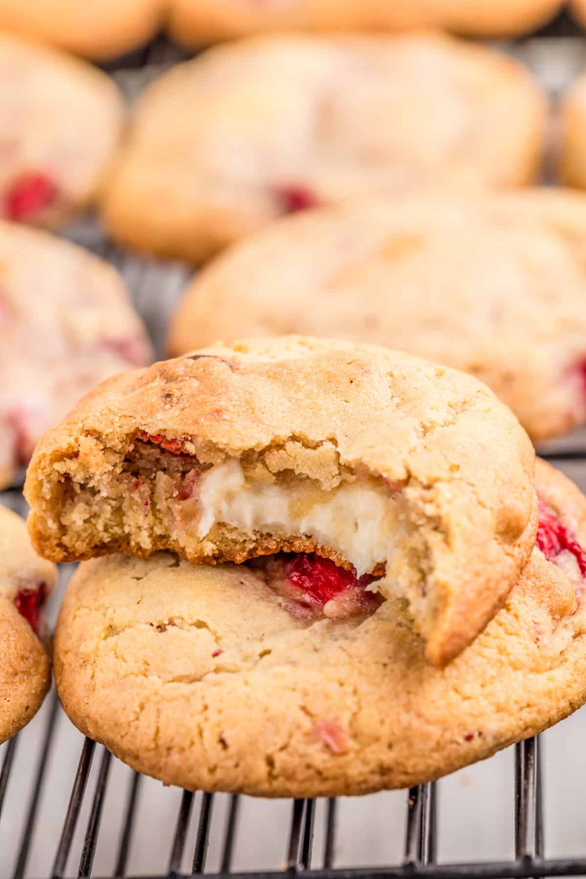 Stacked cookies with a bite taken out of top one showing the cheesecake filling.