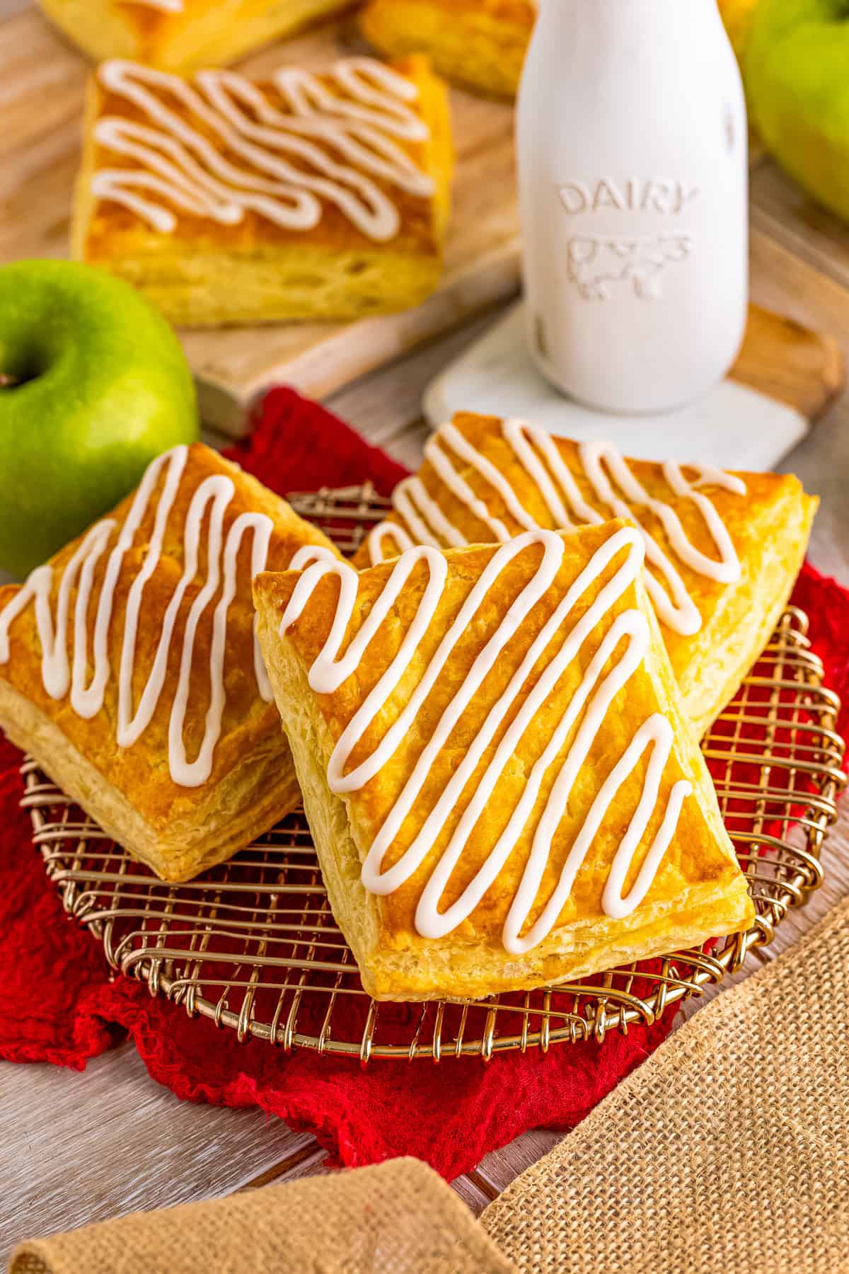 Finished Apple Toaster Strudel with topped with icing with milk and apple behind them.