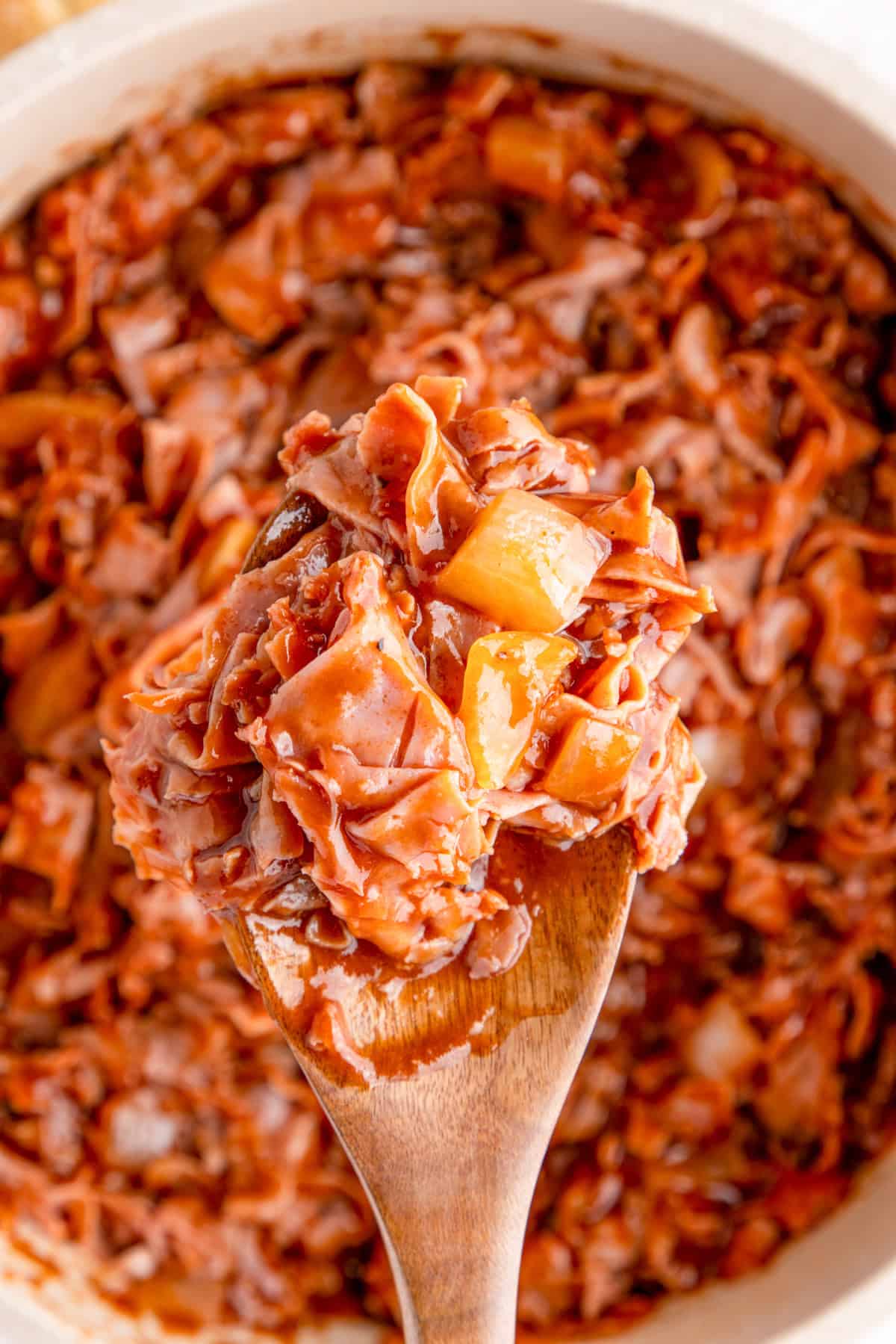 Wooden spoon holding up some chipped ham from pan.