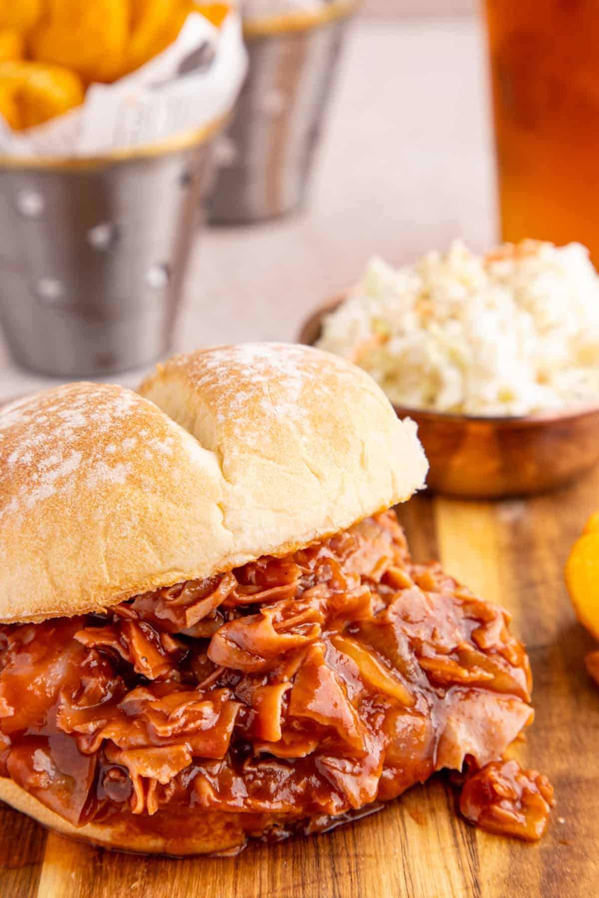 One finished sandwich on wooden platter with meat pouring out of bun.