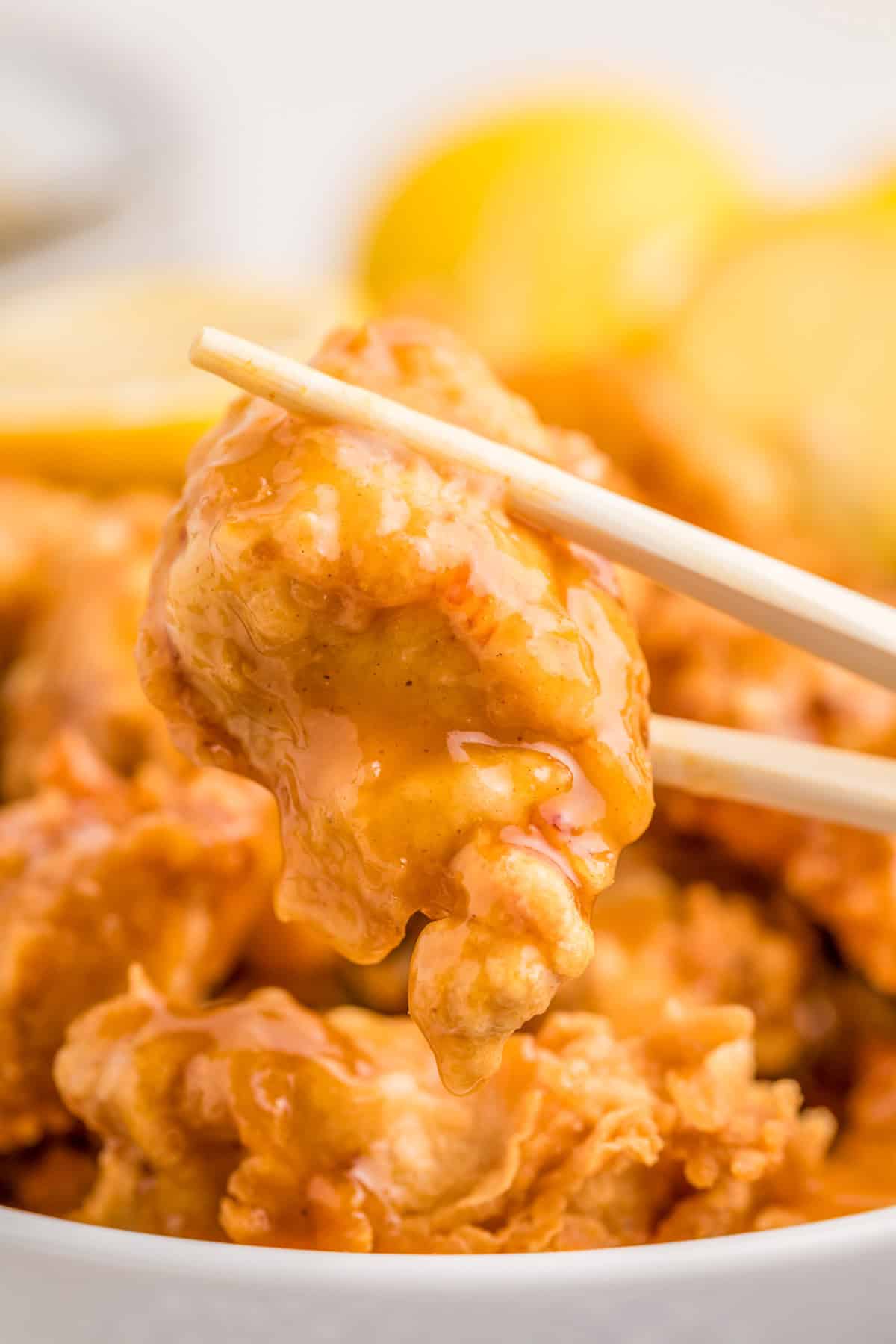 Chopsticks holding up a piece of sauced finished chicken.