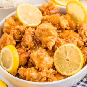 Close up square image of finished chicken with sauce and lemon slices.