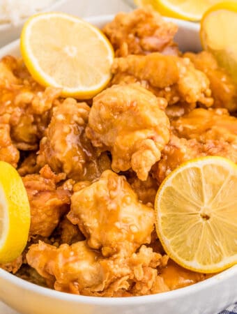Close up square image of finished chicken with sauce and lemon slices.