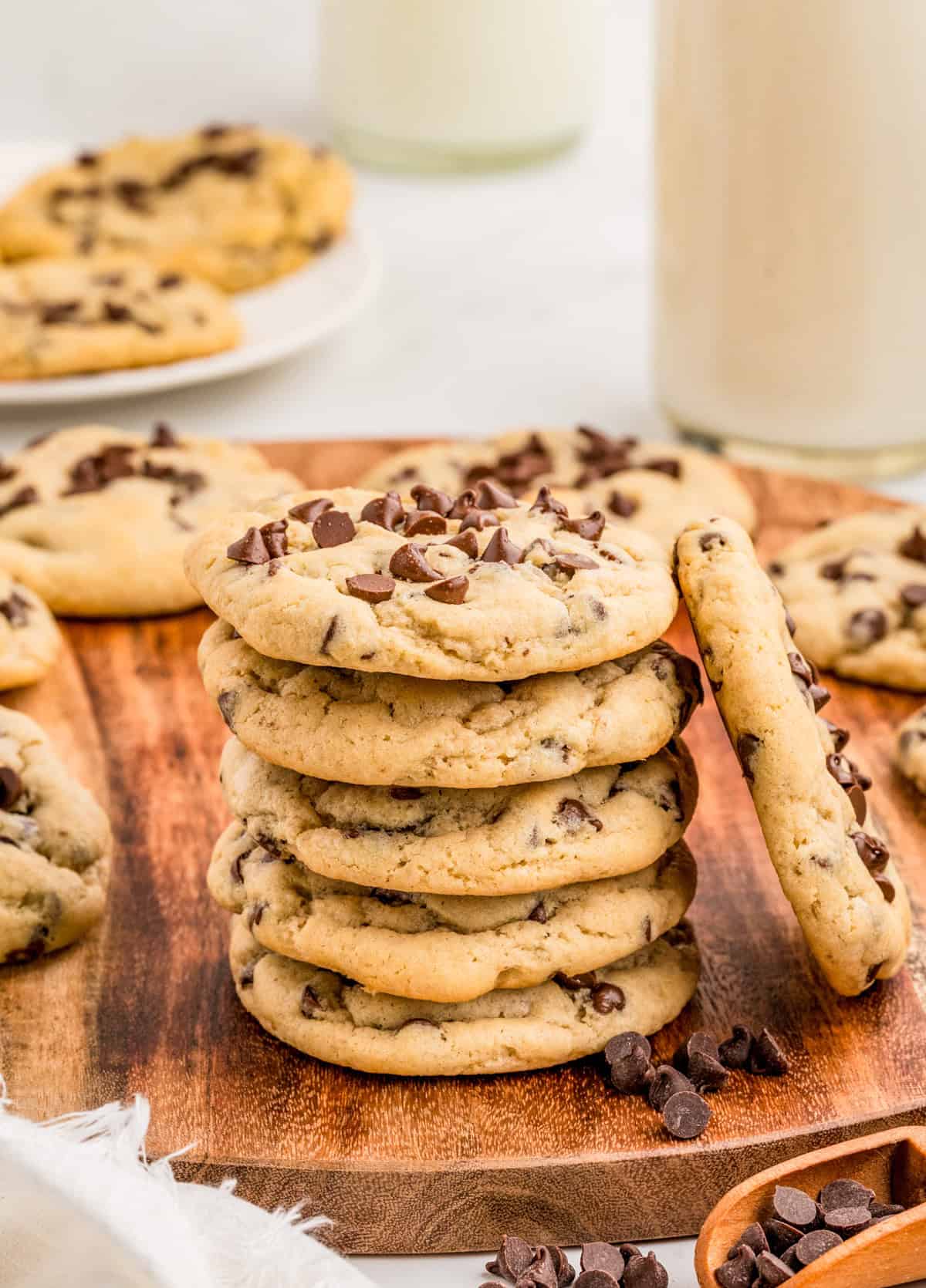 Cream Cheese Chocolate Chip Cookies stacked on wooden board with one cooking leaning against the stack.