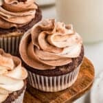 Close up square image of one cupcake on wooden board swirled with chocolate and vanilla frosting.