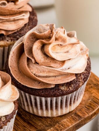 Close up square image of one cupcake on wooden board swirled with chocolate and vanilla frosting.