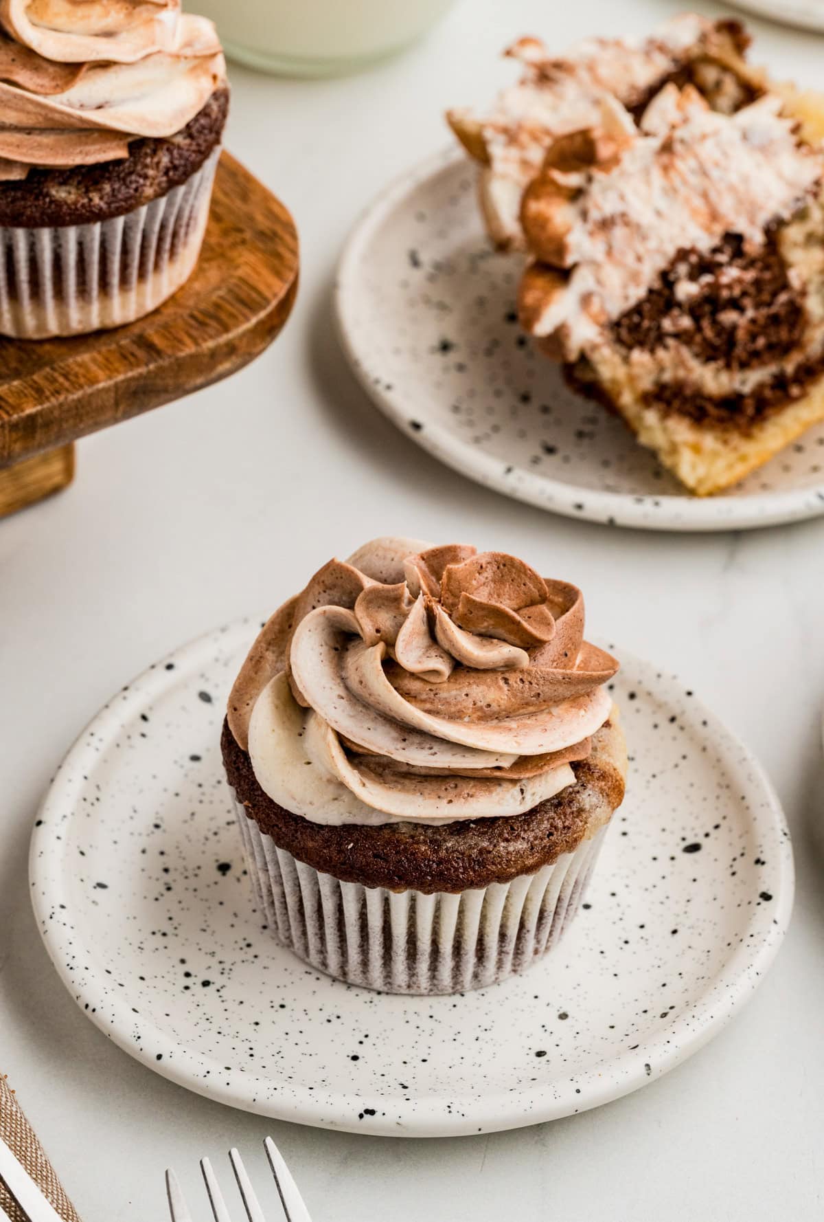 Finished frosted cupcake on plate with cut cupcake in background.