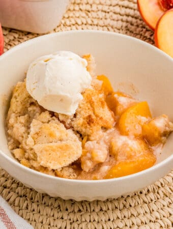 Square image of bowl of cobbler with ice cream scoop.